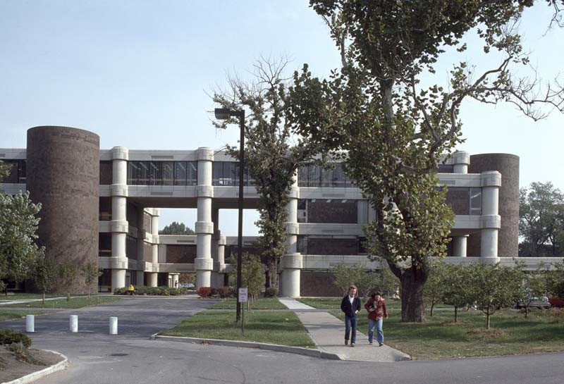 couple walk down sidewalk with Brutalist building in background