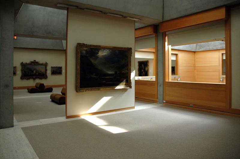 Gallery space with wood partitions, concrete floor with rugs, modular seating and skylights